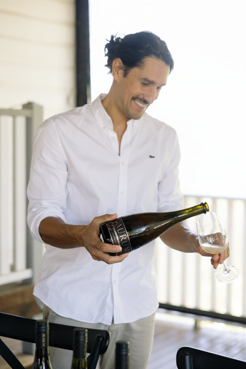 Louis Costa winemaker in a white shirt pouring wine from a bottle into a glass at AURUM Cellar Door